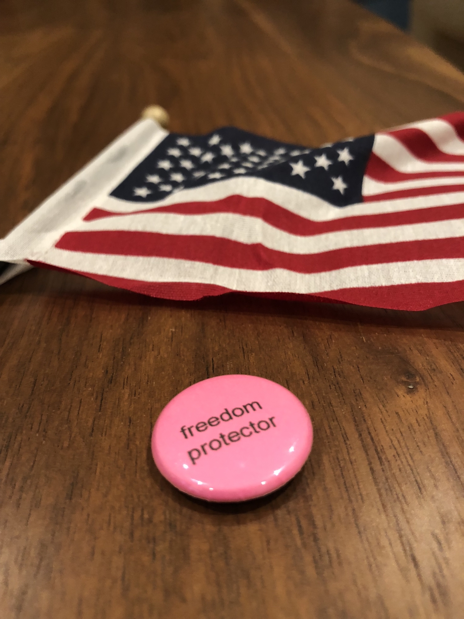 A small american flag and a pink button saying 'freedom protector'